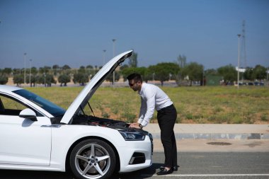 Sakallı yakışıklı genç işadamı yolda bozuk olan arabasının motoruna bakıyor. Adamın acelesi var çünkü işe geç kaldı.