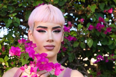 Pembe saçlı ve makyajlı genç eşcinsel çocuk portresinin yanında mor bir bougainvillea çiçeği var. Çocuk farklı ifadeler kullanıyor. Eşitlik ve LGBTQ hakları kavramı