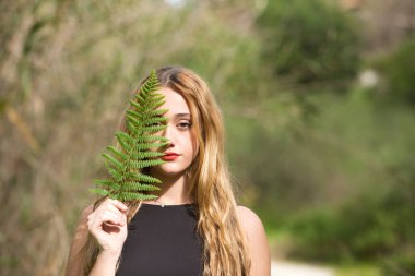 Siyah giyinmiş genç, güzel sarışın bir kadının portresi. Yüzünün yarısı ormanda yeşil bir yaprak ile kaplı. Kadın kendisiyle barışık..