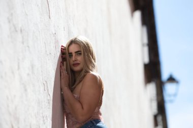 Genç, güzel, mavi gözlü sarışın kadın duvara yaslanıyor ve gündelik, modern kıyafetler giyiyor. Kadın yüzüyle farklı ifadeler kullanıyor, gülümsüyor, ciddi, mutlu ve üzgün.