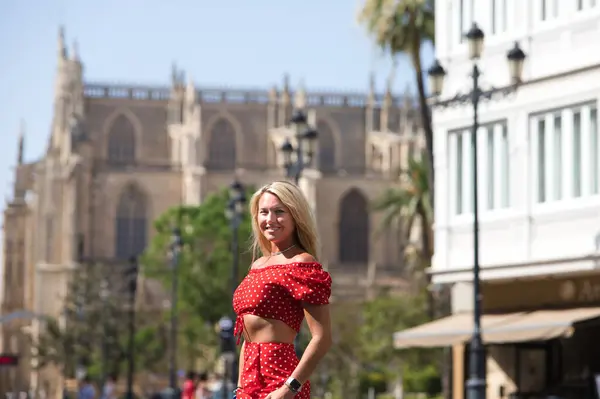 Young and beautiful blonde woman from the United States is on a sightseeing trip to Seville, Spain. The woman is enjoying her holidays in europe. She is between the rails of the urban tram