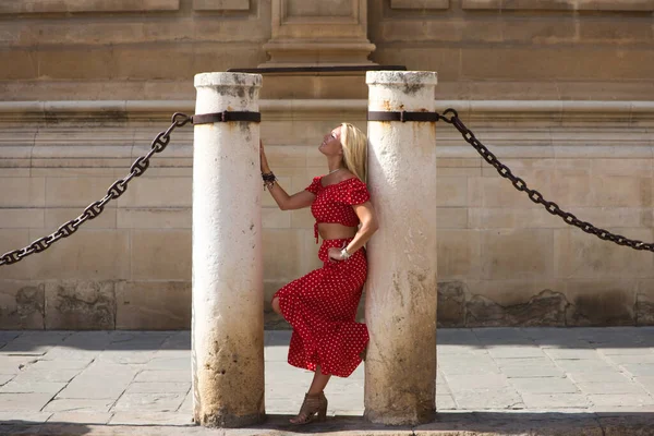 Beautiful young blonde woman from the United States is on a sightseeing trip in Seville, Spain. The girl leans between the columns and chains surrounding the city's gothic-style cathedral