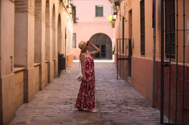 Genç ve güzel sarışın kadın, güneş gözlüğü ve kafasında hasır bir şapkayla Seville 'in tarihi merkezinde yürüyor. Kadın tatilde ve şehrin tadını çıkarıyor. Kadın mutlu.