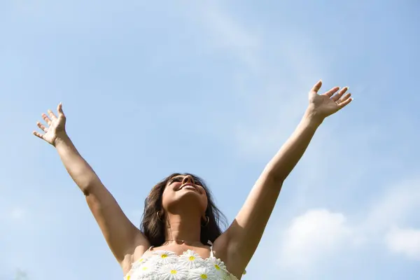 Beautiful Spanish brunette woman with long curly hair raises her arms to the blue sky. The woman is happy and thanks god and life for every day. Concept happiness and thankfulness