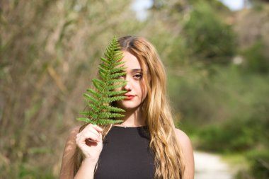 Siyah giyinmiş genç, güzel sarışın bir kadının portresi. Yüzünün yarısı ormanda yeşil bir yaprak ile kaplı. Kadın kendisiyle barışık..