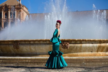 Kafasında çiçek olan yeşil fırfırlı takım elbiseli güzel bir genç kadın. Kadın flamenko yapıyor ve İspanya 'nın en ünlü meydanında merkez çeşmesinin önünde.