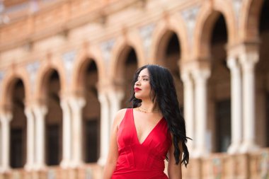 Kısa kırmızı elbiseler ve kırmızı ayakkabılar giyen genç ve güzel esmer kadın Seville, İspanya, uluslararası anıt meydanını ziyaret ediyor ve farklı filmlerin çekildiği