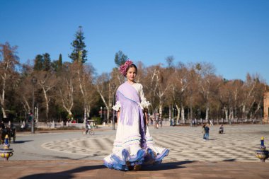 İspanya 'da, Seville' de ünlü bir meydanda bej renkli bir elbise ve fırfırlı mor bir elbise içinde flamenko dansı yapan küçük bir kız. Kızın kafasında çiçekler var ve saçı topuz gibi.