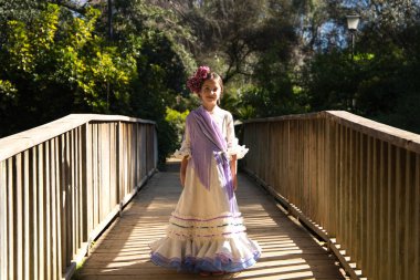 Fırfırlı ve püsküllü tipik bir çingene elbisesi içinde flamenko dansı yapan güzel bir kız İspanya 'nın Seville kentindeki ünlü bir parkta ahşap bir köprüde yürüyor. Saçları bir çiçekle bağlanmış.