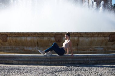 Gündelik giysiler içinde genç ve güzel bir kadın Sevilla 'daki ünlü Plaza de Espana' yı ziyaret ediyor. Kadın Avrupa 'nın eski şehrinde gezmekten zevk alıyor. Büyük merkez çeşmede oturuyor.