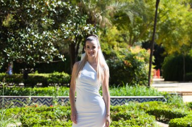 Uzun sarı saçlı ve kısa beyaz elbiseli genç ve güzel bir kadın Seville 'de zengin bir parkta bitki örtüsü, İspanya' da. Seyahat ve tatil konsepti