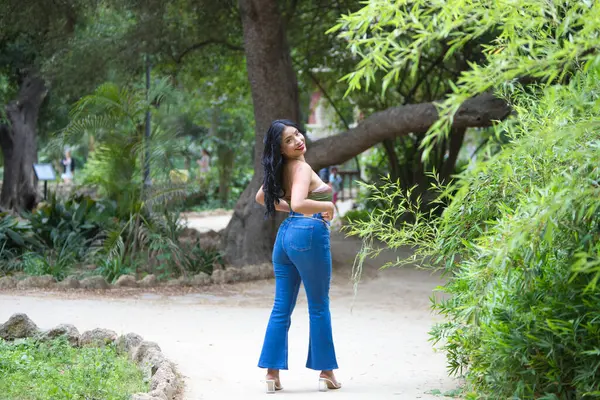 Young and beautiful brunette woman, latin from south america walks among the trees and vegetation of the park. The woman is smiling and happy and is posing with her back to the photos.