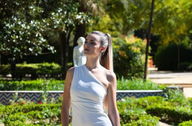 Uzun sarı saçlı ve kısa beyaz elbiseli genç ve güzel bir kadın Seville 'de zengin bir parkta bitki örtüsü, İspanya' da. Seyahat ve tatil konsepti