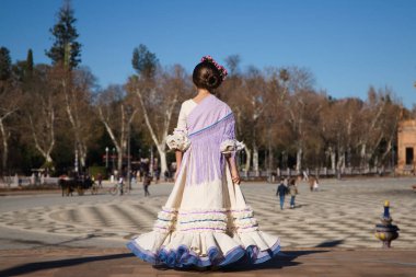İspanya 'da, Seville' de ünlü bir meydanda bej renkli bir elbise ve fırfırlı mor bir elbise içinde flamenko dansı yapan küçük bir kız. Kızın kafasında çiçekler var ve saçı topuz gibi.