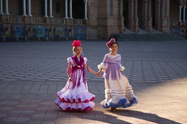 Tipik çingene kostümleriyle flamenko yapan iki güzel kız Sevilla 'da ünlü bir meydanda el ele yürüyorlar. Kızlar çok mutlu. Flamenko, insanlığın kültürel mirası.