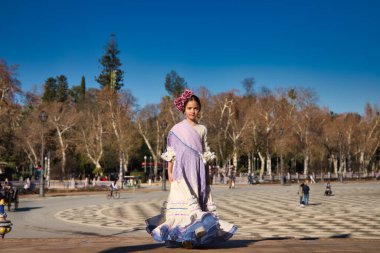 İspanya 'da, Seville' de ünlü bir meydanda bej renkli bir elbise ve fırfırlı mor bir elbise içinde flamenko dansı yapan küçük bir kız. Kızın kafasında çiçekler var ve saçı topuz gibi.