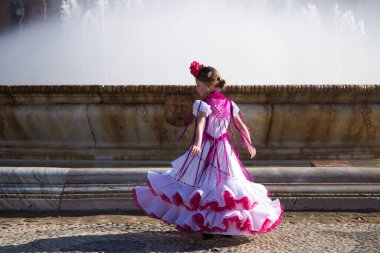 İspanya, Seville 'de ünlü bir meydanda pembe fırfırlar ve püsküllerle beyaz bir elbise içinde flamenko dansı yapan güzel bir kız. Kızın saçında bir çiçek var. Arka planda büyük bir çeşme var.