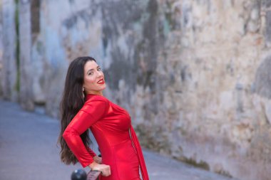 Makyajlı ve zarif kırmızı bir elbise giymiş güzel, genç İspanyol esmer kadın. Kız ellerini korkuluklara dayar ve saçı havada başını geriye doğru uzatır.