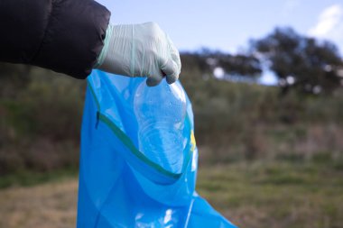 Ormandan plastik şişeyi alıp plastik torbaya koyan bir gönüllü elinin ayrıntıları. Dünya Günü ve Dünya Çevre Günü kavramı 5 Haziran.