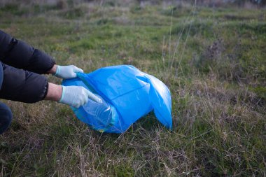 Ormandan plastik şişeyi alıp plastik torbaya koyan bir gönüllü elinin ayrıntıları. Dünya Günü ve Dünya Çevre Günü kavramı 5 Haziran.