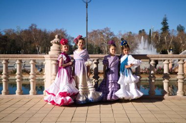 Dört güzel kız tipik çingene kostümü giymiş flamenko dansı yapıyor Seville, İspanya 'da ünlü bir meydanda poz veriyorlar. Arka planda büyük bir çeşme var. Flamenko, insanlığın kültürel mirası.