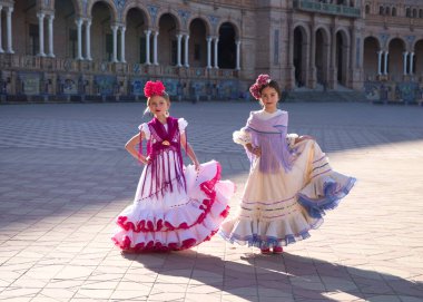 Tipik çingene kostümü içinde flamenko dansı yapan iki güzel kız Seville 'deki ünlü meydanda tek elle elbiselerini tutuyorlar. Flamenko, insanlığın kültürel mirası.