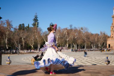 İspanya 'da, Seville' de ünlü bir meydanda bej renkli bir elbise ve fırfırlı mor bir elbise içinde flamenko dansı yapan küçük bir kız. Kızın kafasında çiçekler var ve saçı topuz gibi.