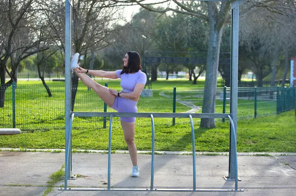 Kısa saçlı ve spor giyinen Latin esmer kadın. Genç ve güzel kız parkta bir eğitim gününden sonra bacağı yukarıda esniyor. Sağlık ve spor kavramı