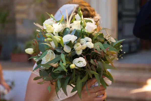 bride with bouquet of flowers covers her face