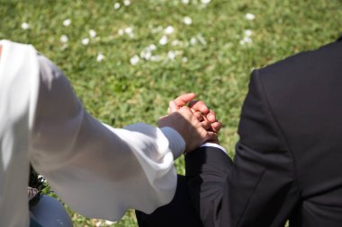 Gelin ve damat gibi giyinmiş, siyah takım elbiseli, beyaz takım elbiseli yeni evli çiftin elleri. Fotoğraf arkadan çekilmiş.