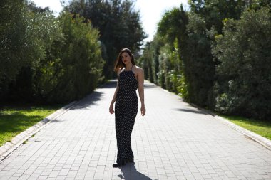 Genç ve güzel bir kadın, esmer ve siyah elbiseli, beyaz benekli, yolda fotoğraf çekimi için poz veren, makyajlı ve kırmızı rujlu bir kadın.