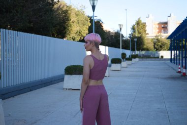 Pembe saçlı ve makyajlı genç eşcinsel adam sokakta yürüyor ve fotoğraf için poz veriyor. Çocuk modern kıyafetlerle pembe giyinmiş. Eşitlik ve LGBTQ hakları kavramı