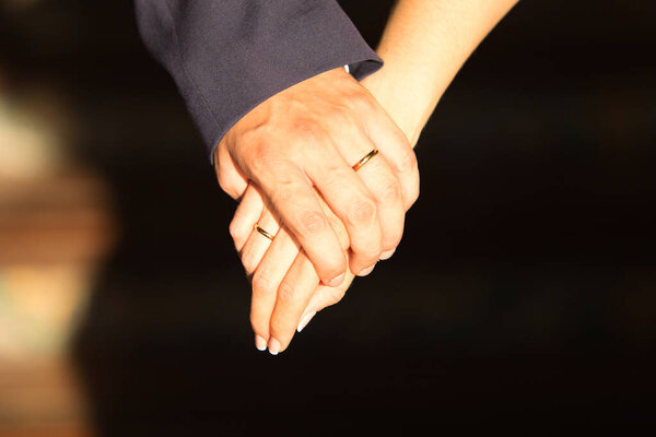 Руки молодоженов переплетались, показывая обручальные кольца против контрастной одежды, символизируя единство и любовь.