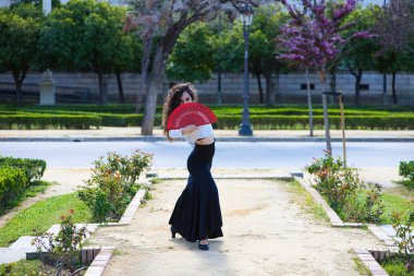 Uzun kıvırcık saçlı, kızıl yelpazeli flamenko dansı yapan güzel bir kadın Sevilla, İspanya 'da. Uzun siyah etek, beyaz gömlek giyiyor ve farklı dans pozları veriyor. İnsanlığın kültürel mirası