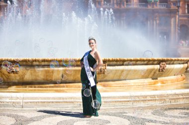 Zarif giyimli ve elmas kaplama takan bir güzellik yarışmasının genç ve güzel kadın kazananı, Sevilla 'da ünlü plaza de espana' da sabun köpükleri arasındaki merkez çeşmenin önünde.