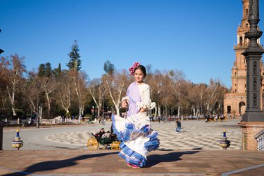 İspanya 'da, Seville' de ünlü bir meydanda bej renkli bir elbise ve fırfırlı mor bir elbise içinde flamenko dansı yapan küçük bir kız. Kızın kafasında çiçekler var ve saçı topuz gibi.