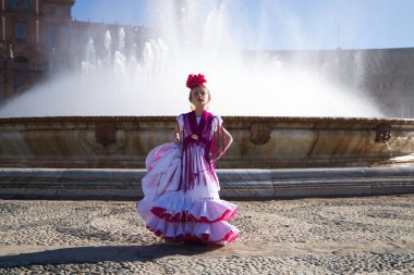 İspanya, Seville 'de ünlü bir meydanda pembe fırfırlar ve püsküllerle beyaz bir elbise içinde flamenko dansı yapan güzel bir kız. Kızın saçında bir çiçek var. Arka planda büyük bir çeşme var.