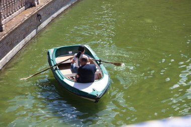 İki turist, bir erkek ve bir kadın, Seville 'deki İspanya meydanındaki kanalda güneşli bir günde kürek çekiyorlar. Seyahat kavramı ve tatil beldesi