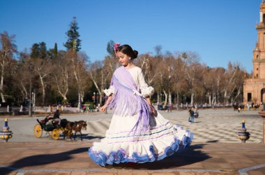 İspanya 'da, Seville' de ünlü bir meydanda bej renkli bir elbise ve fırfırlı mor bir elbise içinde flamenko dansı yapan küçük bir kız. Kızın kafasında çiçekler var ve saçı topuz gibi.