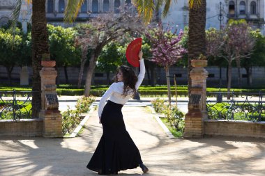 Uzun kıvırcık saçlı, kızıl yelpazeli flamenko dansı yapan güzel bir kadın Sevilla, İspanya 'da. Uzun siyah etek, beyaz gömlek giyiyor ve farklı dans pozları veriyor. İnsanlığın kültürel mirası