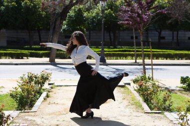 Uzun kıvırcık saçlı güzel bir kadın Seville, İspanya 'da bir parkta ustaca flamenko dansı yapıyor. Uzun siyah etek ve beyaz gömlek giymişti. Flamenko, insanlığın kültürel mirası.