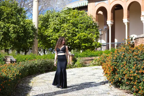 Uzun kıvırcık saçlı güzel bir kadın Seville, İspanya 'da bir parkta yürüyor. Uzun siyah etek ve siyah bluz giymişti. Kadın flamenko dansçısı ve şehri gezmek için fırsattan istifade ediyor.