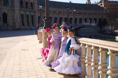 Dört güzel kız tipik çingene kostümü giymiş flamenko dansı yapıyor Seville, İspanya 'da ünlü bir meydanda poz veriyorlar. Yandan çekilmiş bir fotoğraf. Flamenko, insanlığın kültürel mirası.