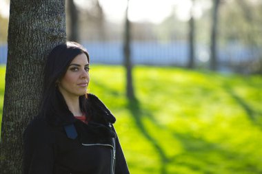 Kısa saçlı, kısa kotlu, siyah ceketli, soğuk bir günde yapraksız ağaca yaslanan genç ve güzel esmer kadın depresyondan dolayı ciddi ve üzgün. Zihin Sağlığı