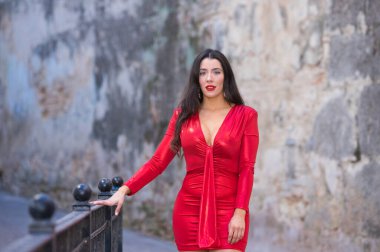 Makyajlı ve zarif kırmızı bir elbise giymiş güzel, genç İspanyol esmer kadın. Kız fotoğraf için korkuluklara yaslanıyor. Mutlu ve gülümsüyor.