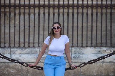 Kot pantolon, beyaz tişört ve güneş gözlüğü giymiş güzel genç bir kadın Seville 'deki gotik katedrali çevreleyen zincirlerde oturuyor. Kadın şehre yaptığı ziyaretten zevk alıyor. Turizm konsepti