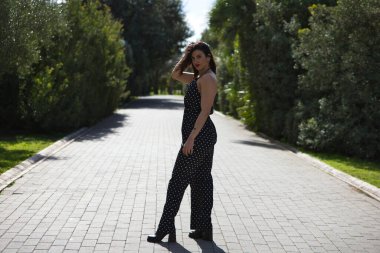 Genç ve güzel bir kadın, esmer ve siyah elbiseli, beyaz benekli, yolda fotoğraf çekimi için poz veren, makyajlı ve kırmızı rujlu bir kadın.