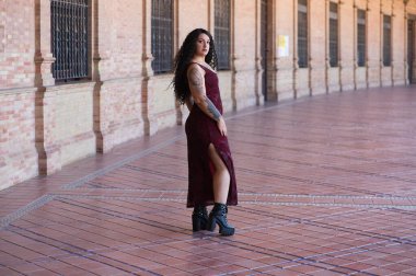 Latin kadın, genç, güzel ve şişman kıvrımlı ve uzun kıvırcık kahverengi saçlı, zarif uzun elbiseli, plaza espana 'nın kemerleri arasında yürüyor farklı pozlar ve duruşlar yapıyor.