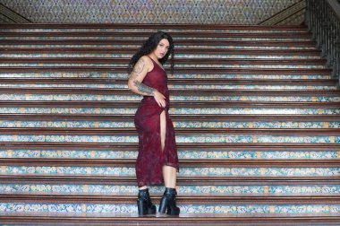 Uzun kıvırcık kahverengi saçlı, genç, güzel ve şişman bir Latin kadın İspanya 'nın ünlü plazasının merdivenlerinde uzun ve zarif bir elbiseyle poz veriyor. Fazla kilolu model konsepti