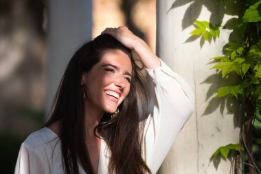 Çok mutlu ve gülümseyen genç ve güzel bir Latin kadının profil portresi. Kızın yüzünün yanında bir bitkinin yeşil yapraklarından dallar var.